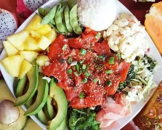 Colorful poke bowl featuring sliced raw ahi tuna topped with green onions and sesame seeds, served with avocado, pineapple chunks, edamame, seaweed salad, and white rice – a vibrant Hawaiian fusion plate.