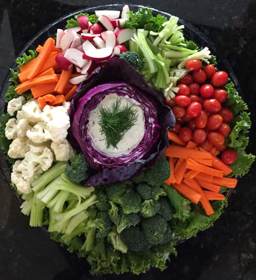 veggie platter with carrots, tomato, broccoli, cauliflower, raddish, and dill dip in the middle