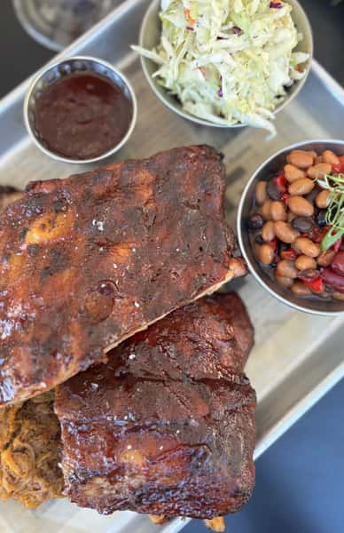 Rack of ribs served with a side of beans and a sauce with salad