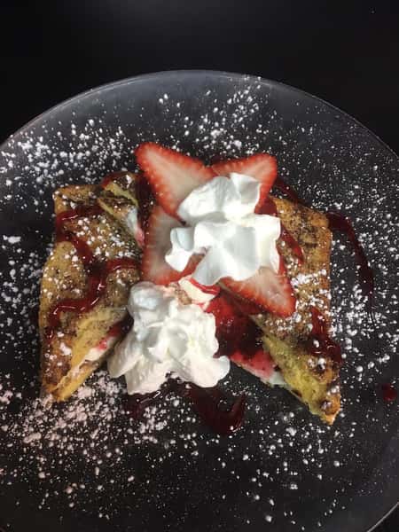 french toast with strawberries, strawberry drizzle, powdered sugar and whipped cream on top