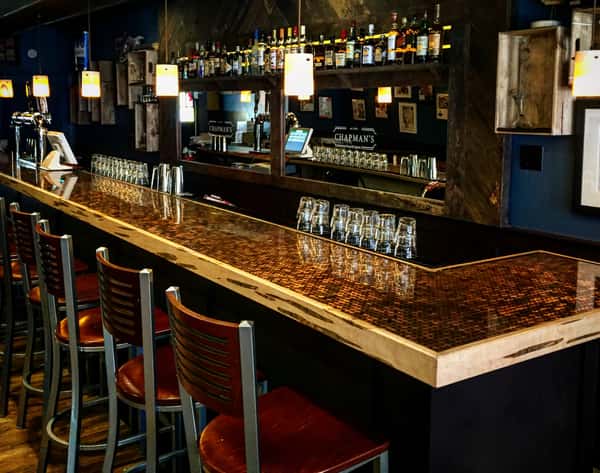 Corner of bar, chairs, liquor bottles behind bar.