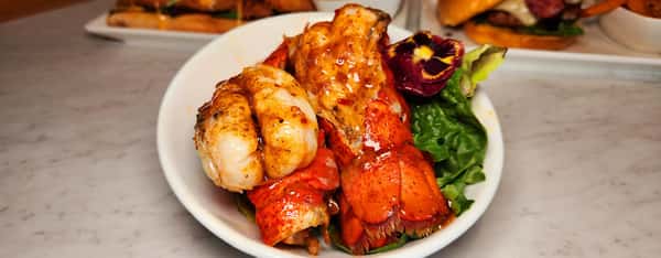 Succulent grilled lobster tails glazed in savory butter sauce, served over a bed of fresh greens and garnished with a vibrant edible flower.