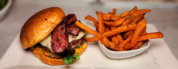 Gourmet bacon cheeseburger on a brioche bun, topped with smoked bacon and fresh greens, served with crispy sweet potato fries.