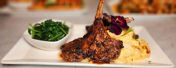 Grilled lamb chops glazed in savory sauce, served with sautéed greens and buttery mashed potatoes, finished with an edible flower.