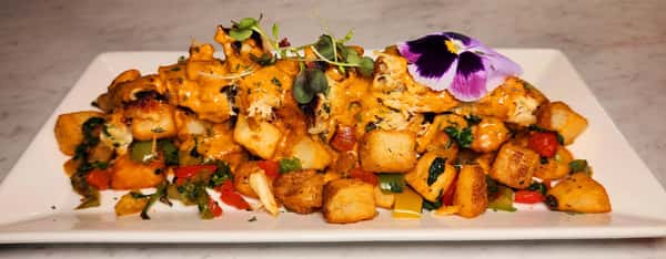 Southern-style breakfast hash with seasoned potatoes, bell peppers, and shredded chicken or crab, drizzled with a creamy sauce and garnished with microgreens and a pansy.