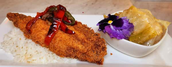 Golden-fried catfish fillet over seasoned white rice, topped with sautéed peppers, served alongside stuffed cabbage rolls and a purple edible flower.