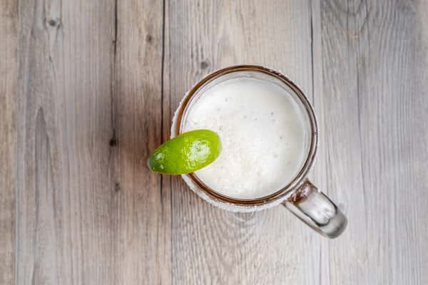 Overhead view of a stein of frothy white beer garnished with a lime wedge, on a wooden table at a restaurant
