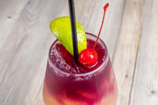 Close-up of a Texas Lady cocktail, a red and orange layered drink garnished with a cherry and lime wedge, in a glass at a restaurant