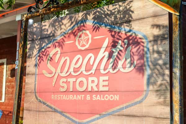 Rustic open-air dining area with wooden picnic tables and historic Texas decor at Spechts Texas Bar & Grill.