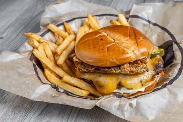 Close-up of Specht's Burger, a cheeseburger with melted cheese on a toasted bun, served with french fries in a metal basket, on a wooden table at a restaurant