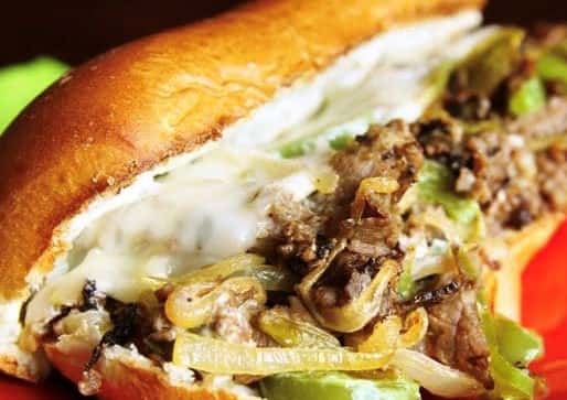 steak slices on a roll topped with peppers and cheese with a side of fries