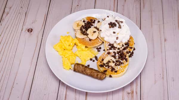 Four mini buttermilk pancakes filled with chocolate chips and topped with banana, served with 1 scrambled egg, 1 bacon or 1 sausage