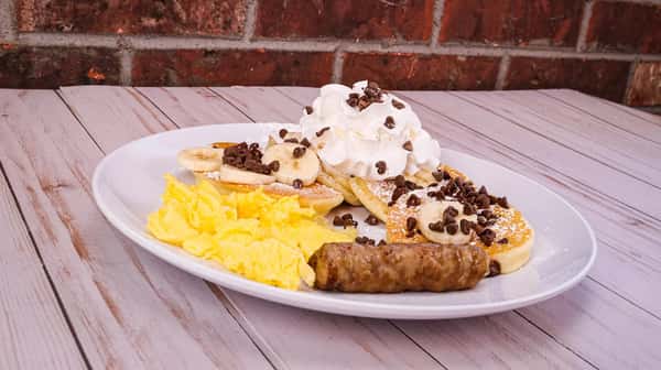 Four mini buttermilk pancakes filled with chocolate chips and topped with banana, served with 1 scrambled egg, 1 bacon or 1 sausage