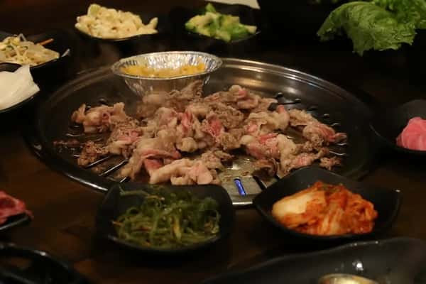 Korean BBQ with sliced beef grilling at the table, surrounded by side dishes like kimchi, seaweed salad, and vegetables.