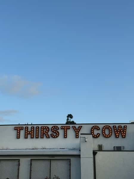 Thirsty Cow restaurant exterior with marquee-style illuminated sign against a clear blue sky.