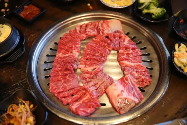 Close-up of marbled raw beef slices neatly arranged on a black plate, prepared for Korean BBQ grilling.