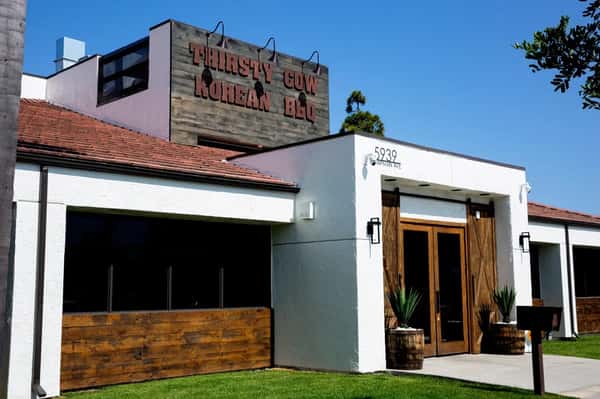 Thirsty Cow Korean BBQ restaurant exterior with white walls, wood accents, and a large wooden sign above the entrance.