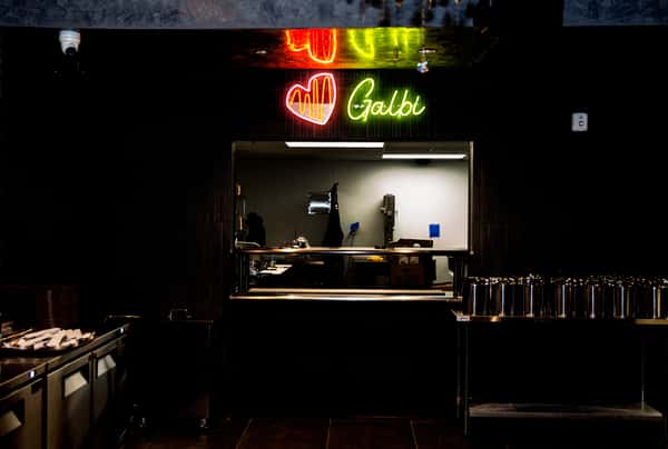 Restaurant kitchen window with neon sign reading "♥ Galbi" in red and green above the serving area.