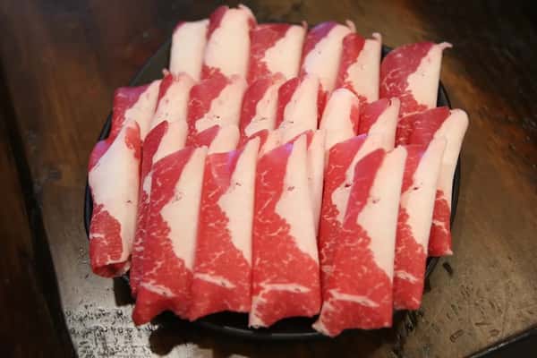 Thinly sliced raw beef rolls arranged neatly on a black plate, ready for Korean BBQ grilling.