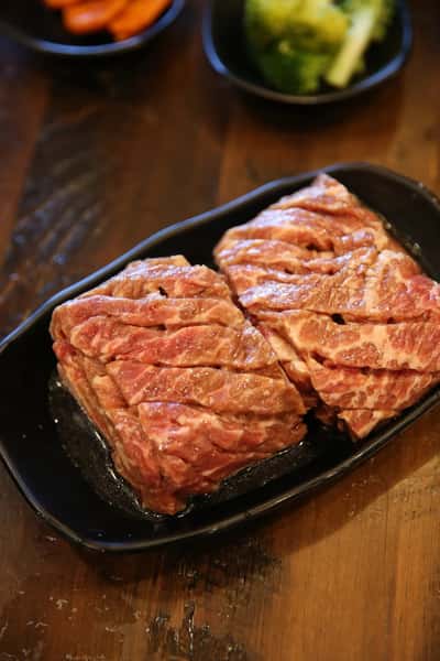 Marinated beef short ribs arranged on a black plate, ready for grilling at a Korean BBQ.