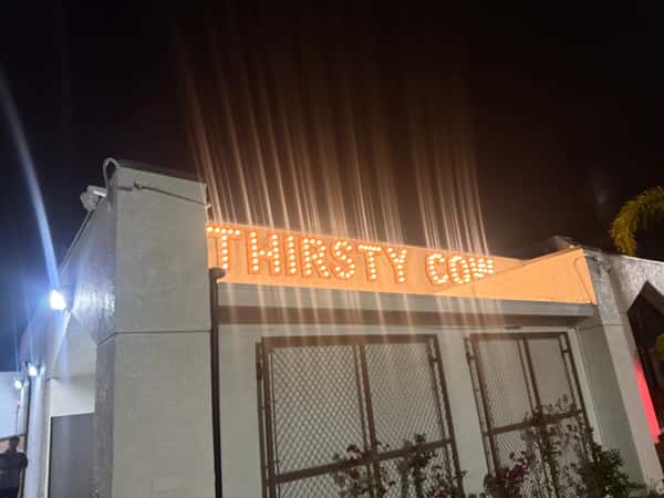 Nighttime view of Thirsty Cow restaurant exterior with illuminated marquee-style sign glowing above the entrance.
