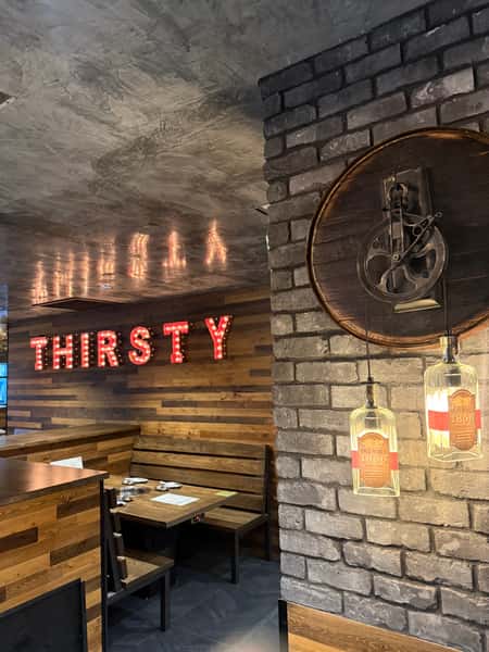 Interior of Thirsty Cow restaurant with marquee-style "THIRSTY" sign, wooden booths, and decorative hanging bottle lights.