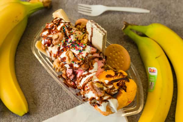 Banana split dessert topped with whipped cream, chocolate drizzle, sprinkles, and bananas