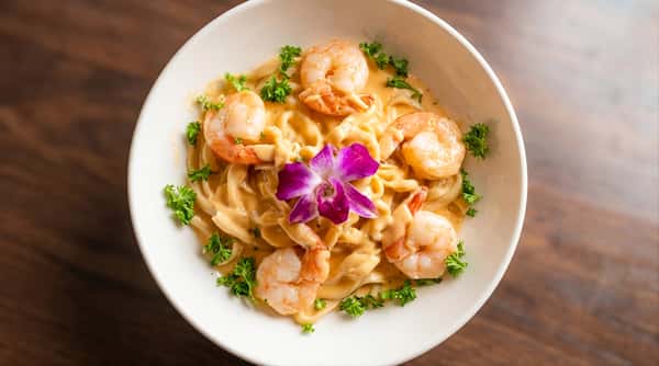 Shrimp pasta served in a white bowl with parsley and a purple orchid garnish.