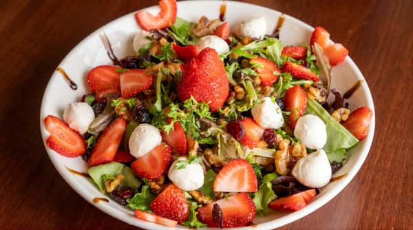 Fresh salad topped with sliced strawberries, mozzarella, and mixed greens.