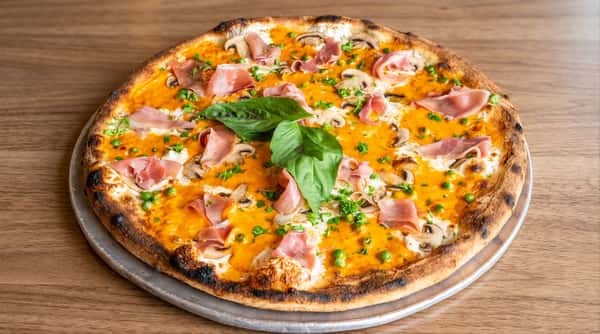 Pizza topped with prosciutto, basil, and melted cheese on a wooden table.