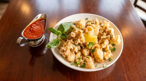 Bowl of creamy pasta topped with grilled chicken and served with marinara sauce on the side.