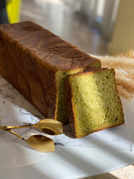 loag of Matcha Boloniya bread next to a set of brass serving tongs