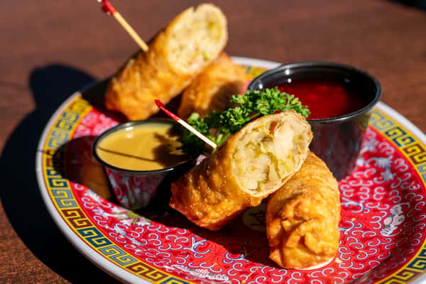 A colorful appetizer platter featuring crispy fried rolls and stuffed pastries, garnished with fresh parsley and served with two dipping sauces. The vibrant presentation and golden fried texture create a festive and savory dining feel.