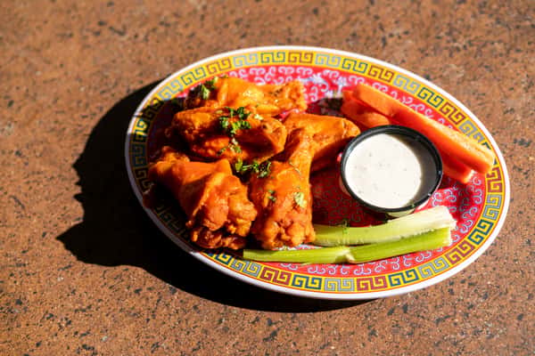 A platter of crispy chicken wings coated in a flavorful glaze, served with a side of creamy dipping sauce. The wings are arranged on a colorful decorative plate, giving the dish a bold and savory presentation.