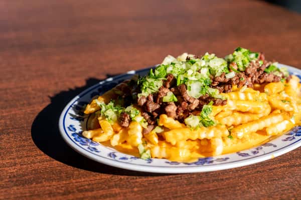 A loaded plate of fries topped with seasoned ground beef, melted cheese, chopped green onions, and creamy sauce. The dish looks rich, indulgent, and packed with bold flavors, perfect for comfort-food lovers.