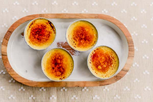 Four individual crème brûlée desserts with caramelized tops on a tray from The Butcher Shop bakery