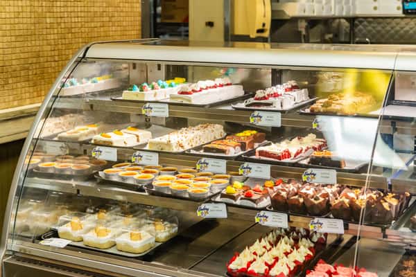 A large bakery display case showcasing a wide variety of cakes and pastries at The Butcher Shop bakery