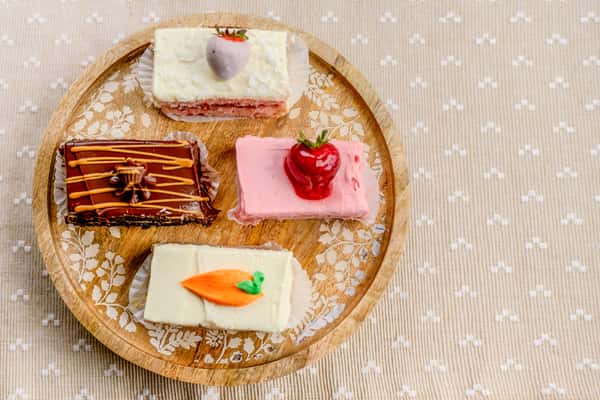 An assortment of decorative petit four cake bars with fruit toppings on a wooden board from The Butcher Shop bakery