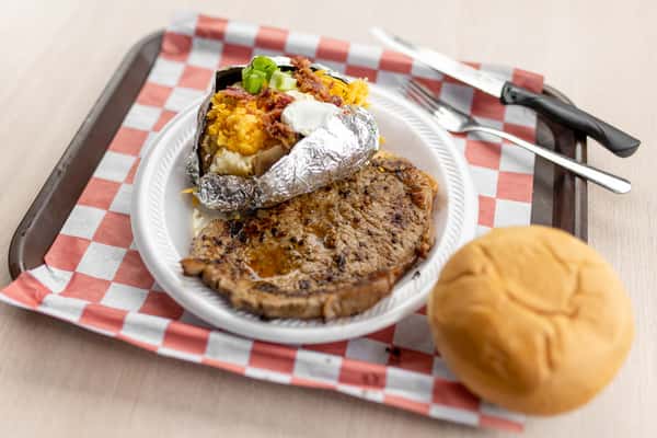 A grilled ribeye steak served with a side and dinner roll on a checkered tray at The Butcher Shop restaurant