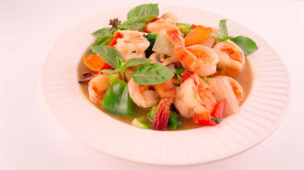 bowl of seafood soup with shrimp, vegetables, and herbs