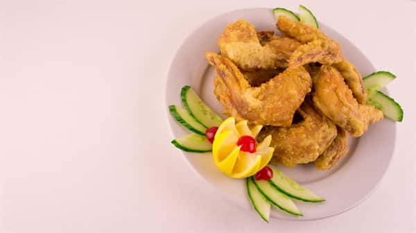 plate of fried chicken wings, garnished with lemon and cucumber