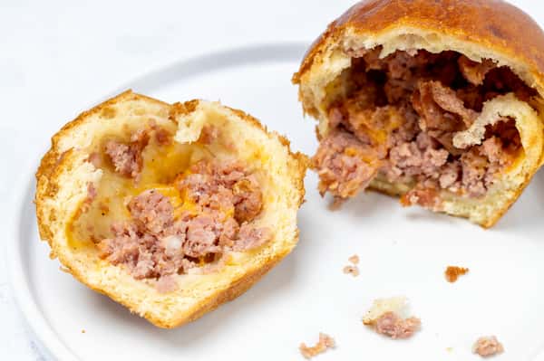 A savory baked bun is cut in half, revealing a filling of meat and cheese. The warm, golden bun suggests a comforting bakery treat.
