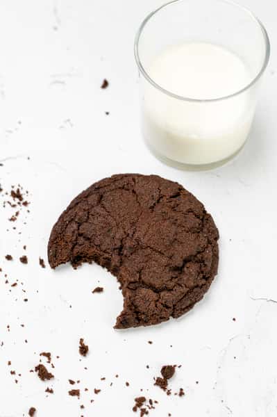 A chocolate cookie sits with a bite missing and a glass of milk. The overhead shot is great for a website's photo gallery.