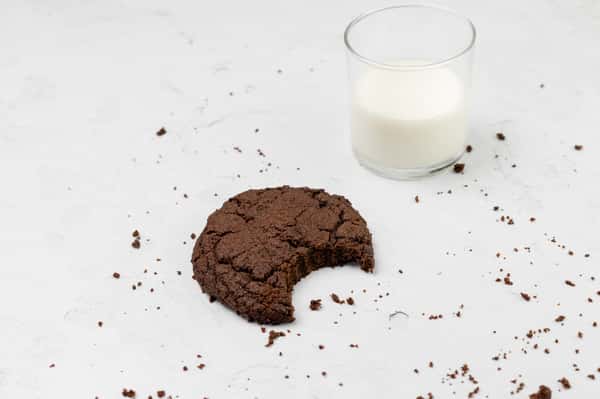 Overhead shot of a chocolate cookie with a bite taken out, and a glass of milk. The image invokes a sense of comfort and indulgence.