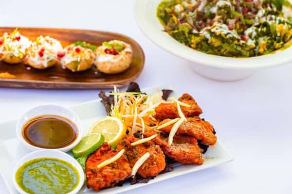 Crispy fish pakora with lemon wedges, green and tamarind chutneys, served with dahi puri and a leafy spinach chaat bowl.