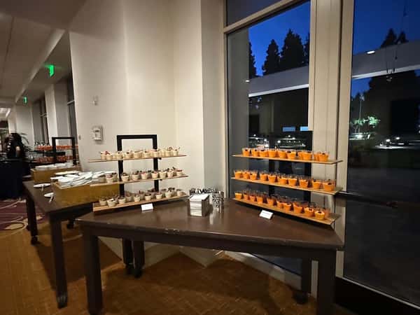 Assorted desserts displayed on tiered trays near large windows during an evening event with a view of trees and outdoor lights.