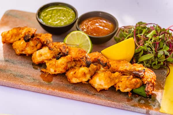 Tandoori grilled shrimp skewers served with lemon wedges, microgreens, and green and red dipping sauces.