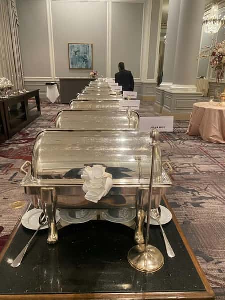 Buffet line with silver chafing dishes labeled with Indian dishes like Jeera Rice and Vegetable Biryani in an elegant banquet hall.
