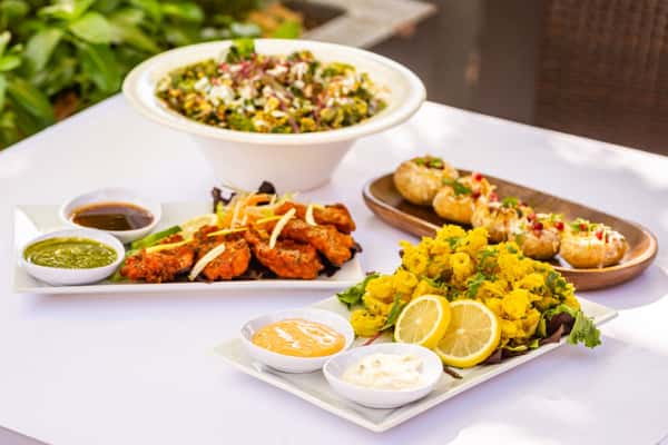 Indian appetizers including crispy pakoras, grilled chicken, pani puri, and a large mixed salad served with chutneys and dips.