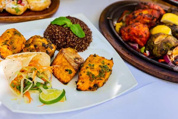 Tandoori grilled paneer cubes served with quinoa, salad, and lemon wedge on a white plate with sizzling mixed grill nearby.